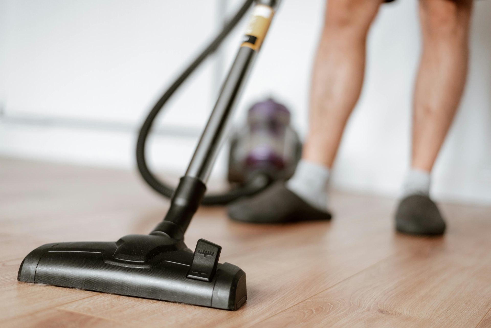 A person uses a vacuum cleaner on a wooden floor for effective cleaning.